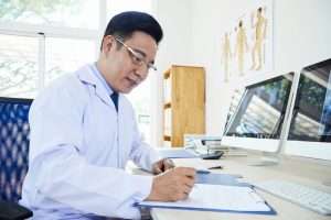 doctor sitting at desk doing paperwork, outsourced medical billing concept